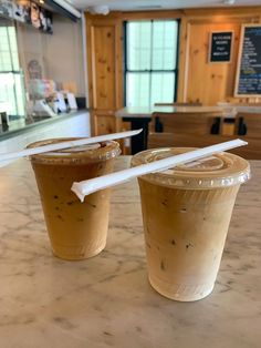 two plastic cups sitting on top of a counter next to each other with straws sticking out of them