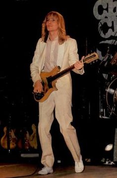 a man standing on stage with a guitar in his hand and wearing a white suit