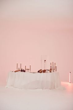 the table is set up with candles and desserts on it in front of a pink wall