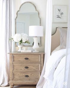 a bedroom with a bed, mirror and flowers on the dresser in front of it