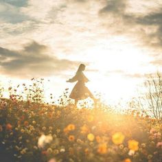 a woman is walking through a field full of wildflowers and the sun shines brightly in the background