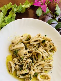 pasta with pesto and parsley on a white plate next to pink flowers in the background