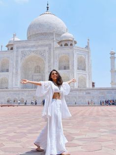 a woman standing in front of a white building with her arms out and hands outstretched