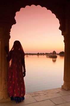 a woman standing in front of a body of water looking at the sunset over it