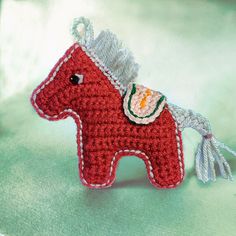 a crocheted red horse ornament on a green surface