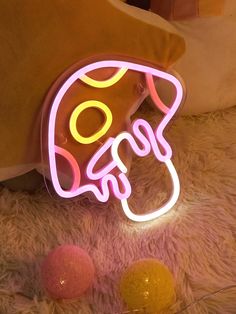 a neon sign sitting on top of a white rug next to balls and a pillow