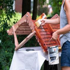 a woman is painting a wooden bench outside