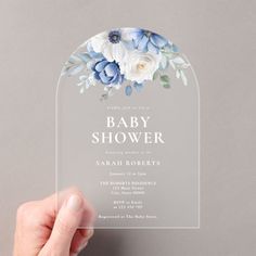 a person holding up a clear plastic baby shower card with blue and white flowers on it