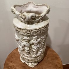 a white vase sitting on top of a wooden table next to a wall and floor