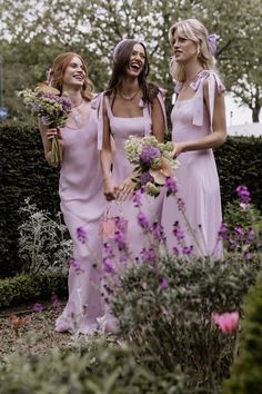 three women in pink dresses standing next to each other holding flowers and smiling at the camera