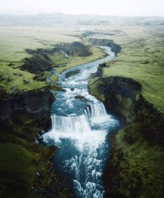 an aerial view of a waterfall in the middle of a green valley with water running through it