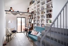 a living room filled with lots of furniture and bookshelves next to a stair case