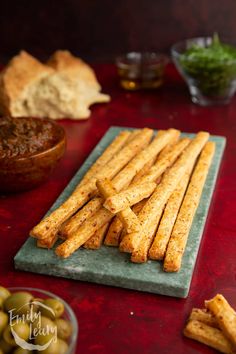 some bread sticks are on a green plate next to olives and pita chips