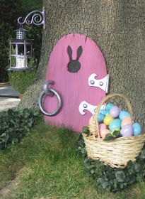 a basket full of eggs next to a tree with a pink door and bunny ears on it