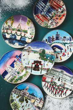 four plates with different designs on them sitting in the snow near water and city buildings