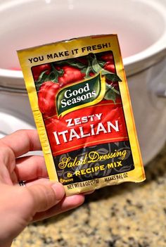 someone holding up a packet of good seasons zesty italian salad dressing in front of a crock pot