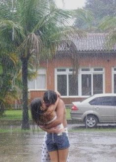 two people hugging each other in the middle of a flooded street with cars behind them