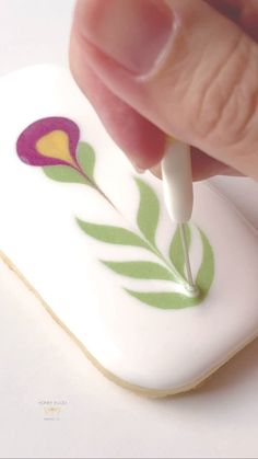 a hand holding a small white object with purple and yellow designs on it's side