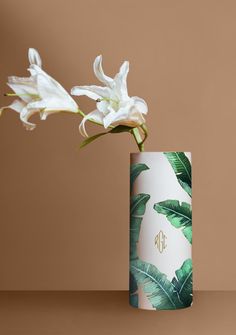 a white flower is in a vase on a table next to a brown wall and a monogrammed background