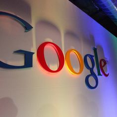 the google logo is lit up in front of a wall with people standing around it