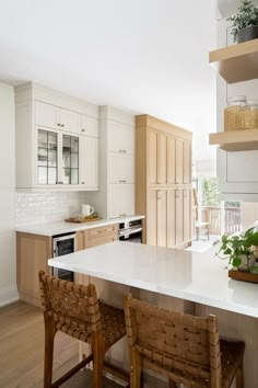 a kitchen with white counter tops and wooden chairs in front of an island that has plants on it