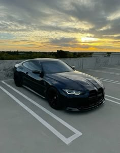 a black sports car parked in a parking lot with the sun going down behind it