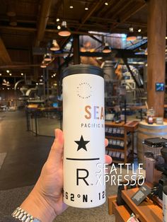 a person holding up a coffee cup in front of the camera at sea pacific seattle