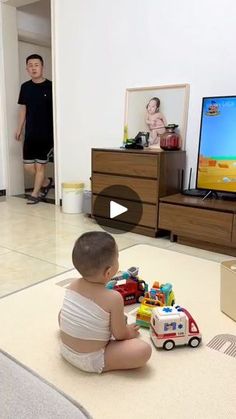 a baby sitting on the floor in front of a tv playing with toy cars and toys