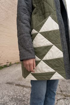 a person standing in front of a brick wall wearing a quilted jacket and jeans