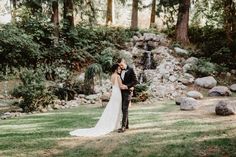 a bride and groom standing in front of a waterfall at their outdoor wedding ceremony venue