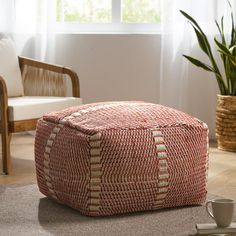 a red and white ottoman sitting on top of a floor next to a potted plant