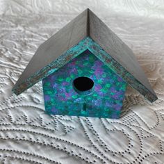 a blue birdhouse sitting on top of a white bed sheet with a black hole in the roof