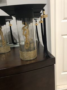 three glass vases with black and gold decorations on top of a wooden table in front of a white door