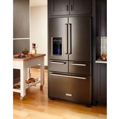 a large stainless steel refrigerator in the middle of a kitchen with wood flooring and black cabinets