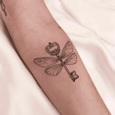 a small dragonfly tattoo on the right arm and leg, with a key attached to it