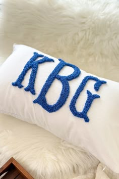 a white pillow with blue letters on it sitting on top of a fur covered bed