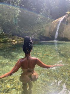 a woman standing in the water with her back turned to the camera and looking at a waterfall