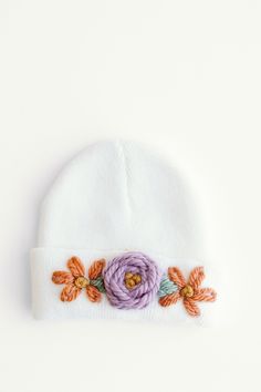 a white beanie with flowers on the front and side, sitting against a white background