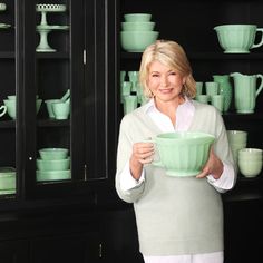 a woman is holding a green bowl in front of shelves with cups and saucers