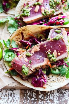 two tacos filled with meat and veggies on top of a cutting board