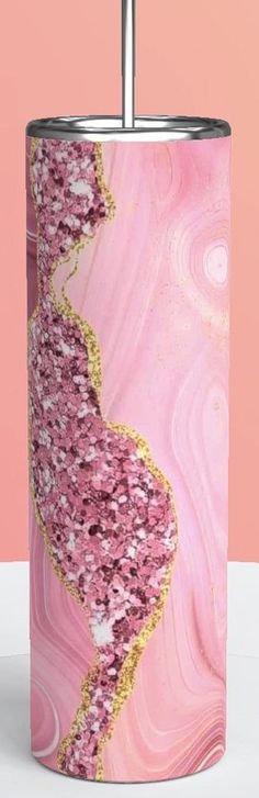 a pink and gold canister with an abstract design on the bottom, in front of a pink background