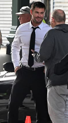 a man wearing a black tie and white shirt talking to another man on the street