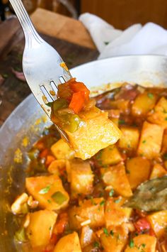 a fork with some food in it on top of a pan filled with potatoes and peppers