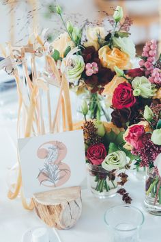 the table is set with flowers in vases and place cards for guests to use