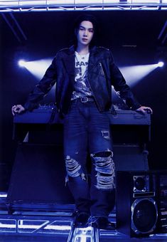 a man standing on top of a stage with his hands in his pockets and wearing ripped jeans