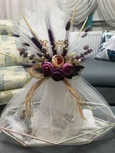 a vase filled with flowers and feathers on top of a glass shelf next to a couch