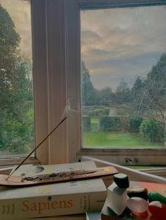 a table with books and vases on it in front of a window overlooking a field