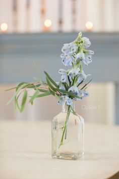 a glass vase with blue flowers in it on a wooden table next to some candles