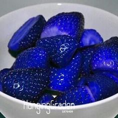 a white bowl filled with blue strawberries on top of a table