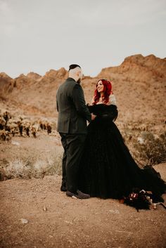 a man and woman dressed in black standing next to each other on a dirt field